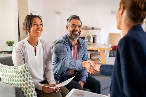 Man and woman smiling and shaking hands with an Indiana lemon law lawyer during a meeting